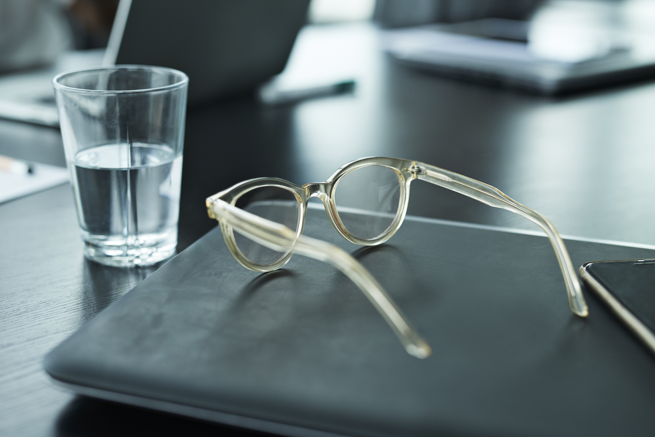 Close-up of spectacles and glass of water on table in meeting room